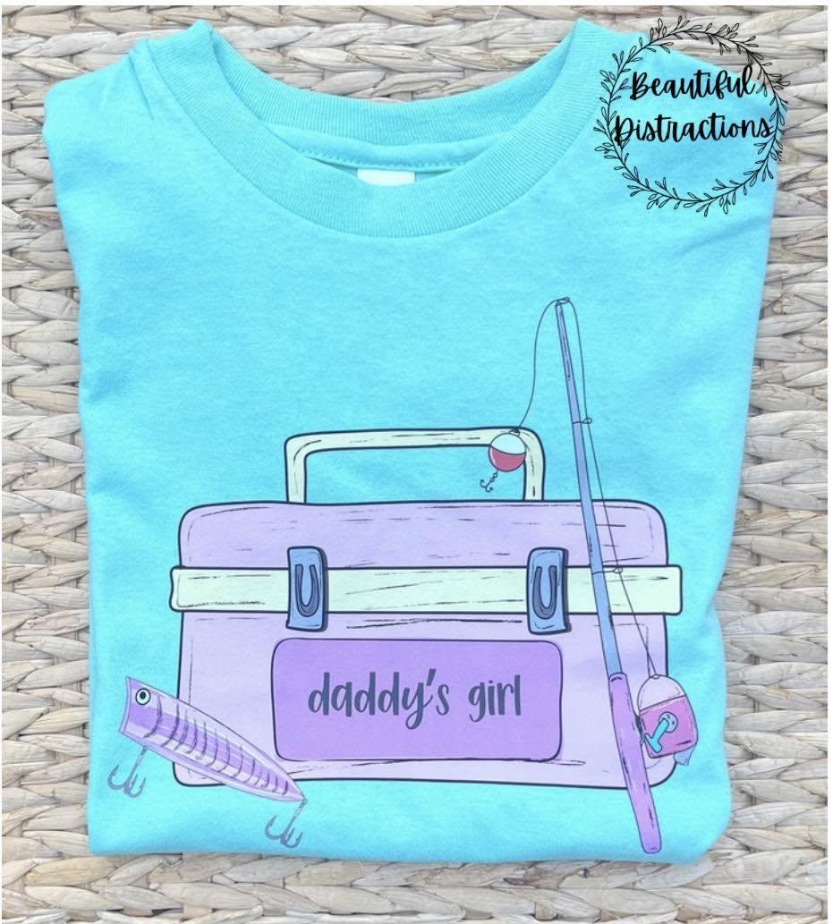 mint color t-shirt with a purple and pink fishing tackle box graphic and 'daddy's girl' text on a woven surface.