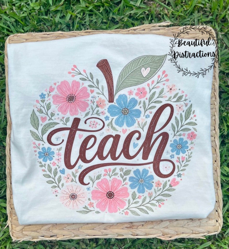 apple design made of florals with the word teach in brown across the middle of it lying on woven surfaced placed in the grass