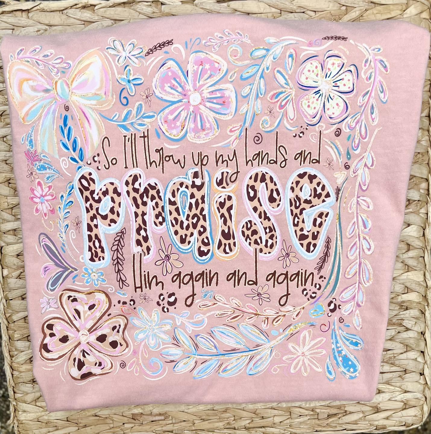 peach color tee with floral and leopard print designs that says so i'll throw up my hands and praise him again and again on a woven surface