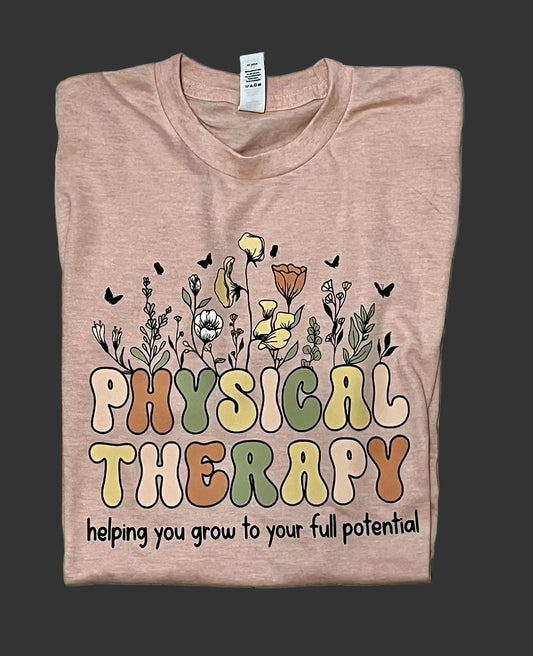 A peach-colored t-shirt with a floral physical therapy design, featuring plant and butterfly graphics, and the text 'PHYSICAL THERAPY HELPING YOU GROW TO YOUR FULL POTENTIAL'.