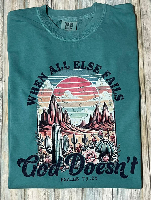 A green t-shirt with a graphic print of a desert landscape at sunset and the text 'God doesn't fail' from Psalms 71:12-16.