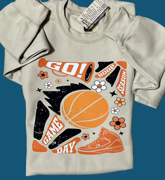 A beige sweatshirt with a basketball and hoop design, including text phrases such as 'GO!', 'HOOP!', 'GAME DAY', and brand-related graphics.
