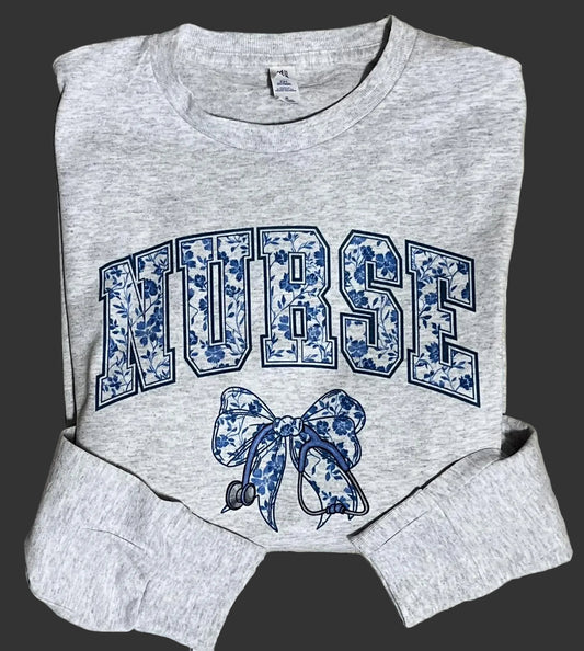 A gray-colored shirt with a floral stethoscope design and the word 'NURSE' written above the design. A bow is also visible on the shirt.