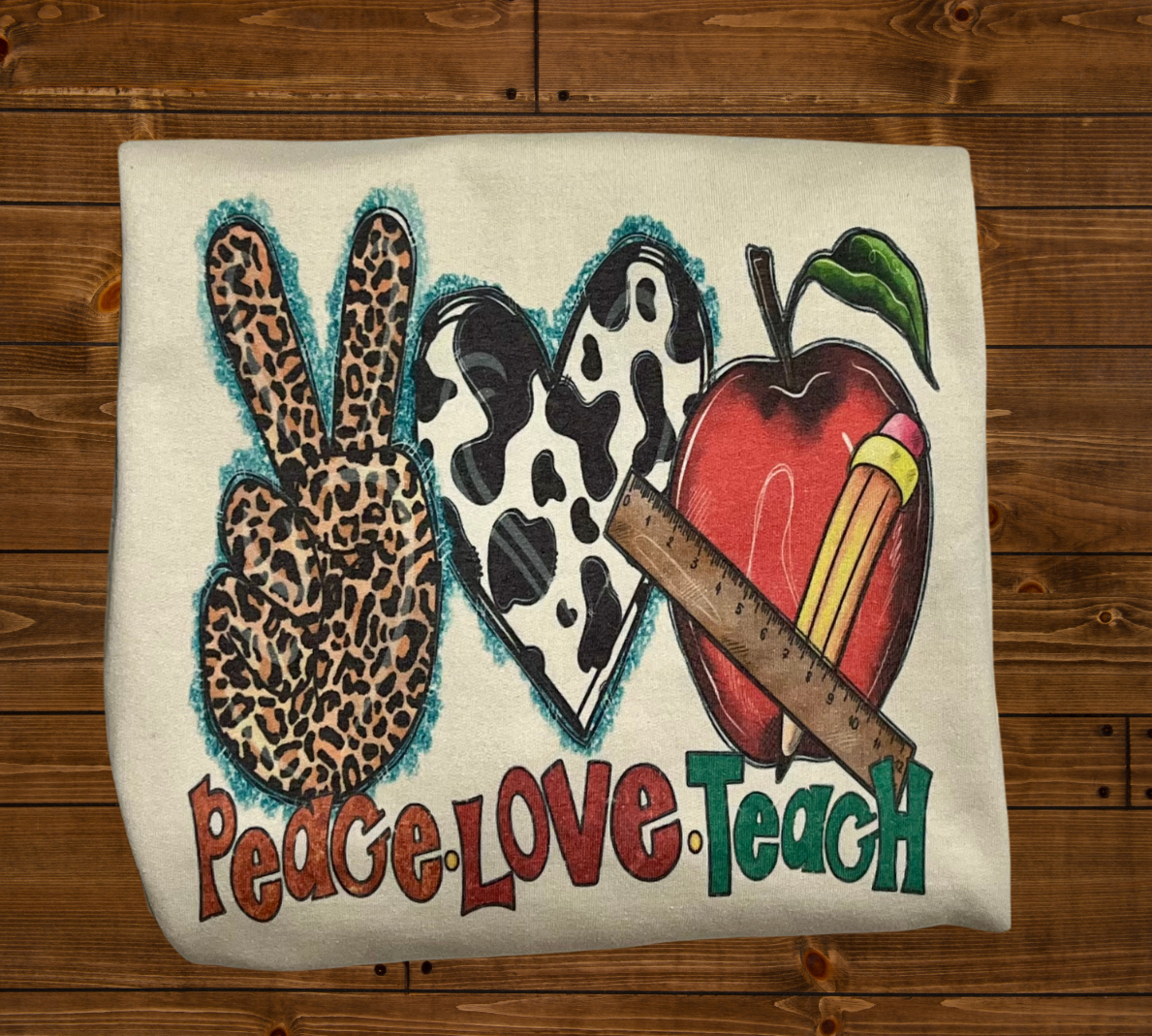 A sweatshirt with a design that includes a peace sign, an apple, and a leopard print pattern, with the text 'PEACE-LOVE-TEACH'.