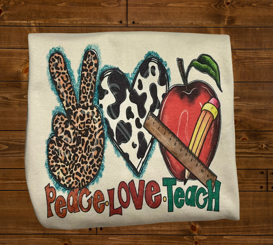 A sweatshirt with a design that includes a peace sign, an apple, and a leopard print pattern, with the text 'PEACE-LOVE-TEACH'.