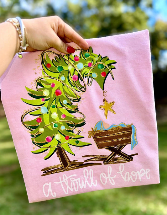 Pink shirt with Christmas tree and nativity design held by a hand outdoors.
