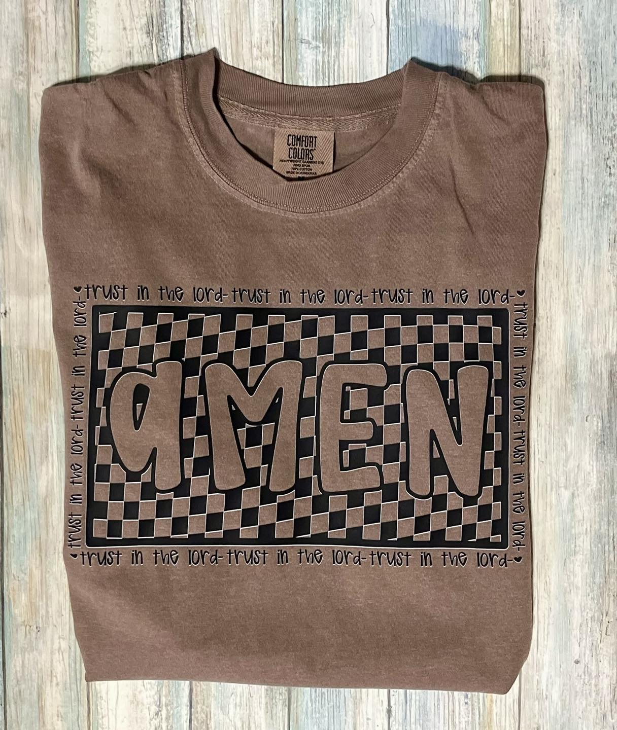 A brown t-shirt with a checkered pattern and the word 'AMEN' printed on the front.