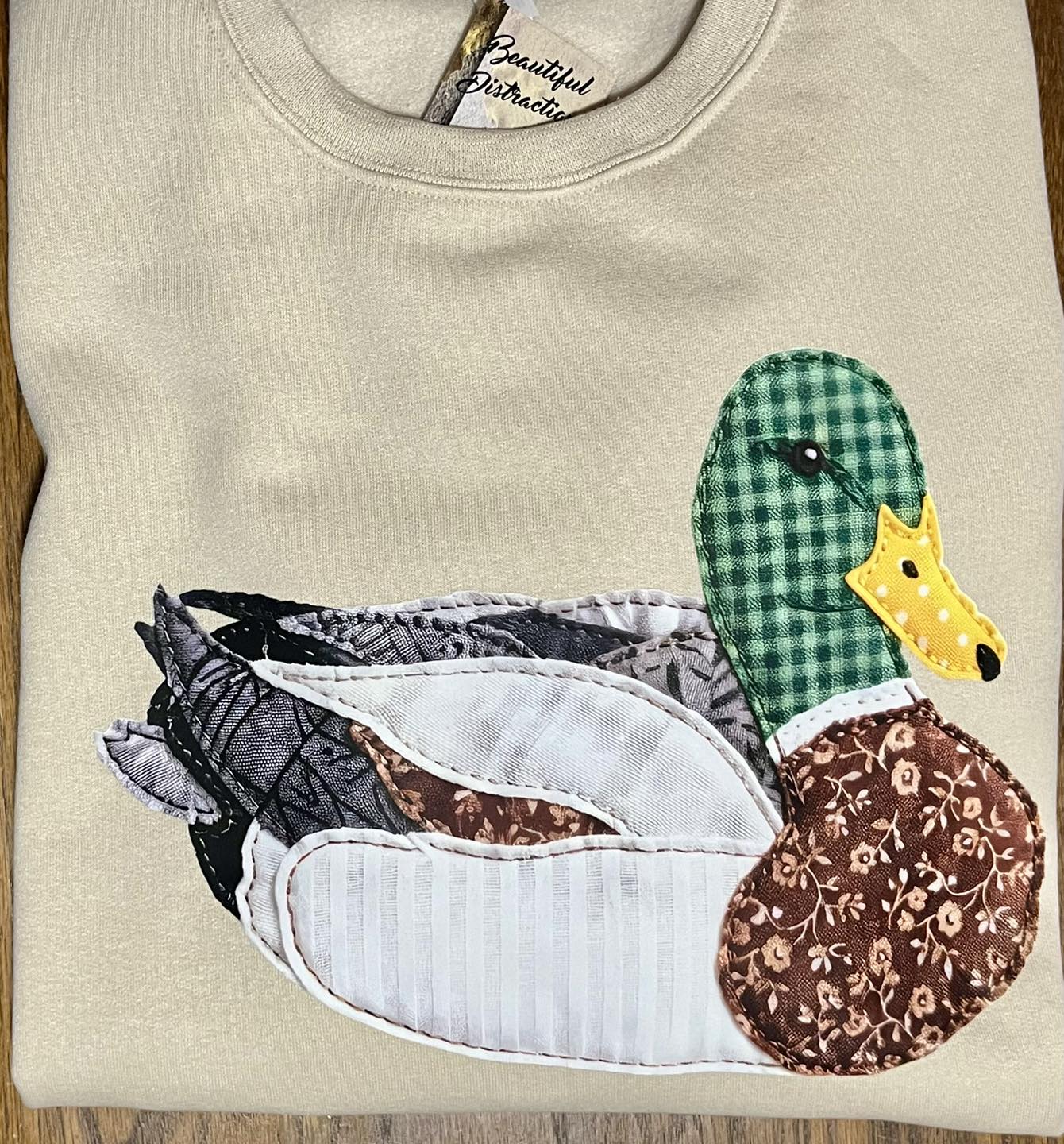 tan sweatshirt with multi color patchwork duck decal on wooden background
