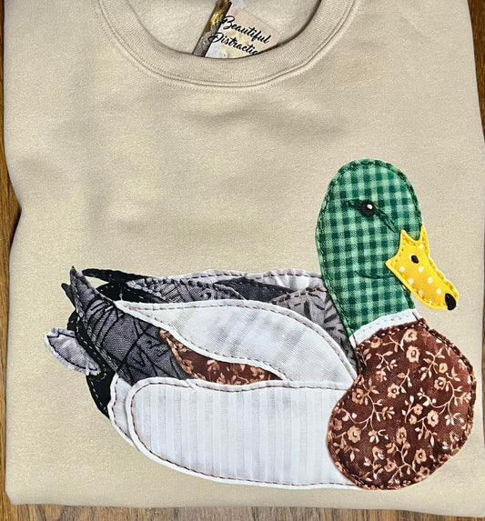 tan sweatshirt with multi color patchwork duck decal on wooden background