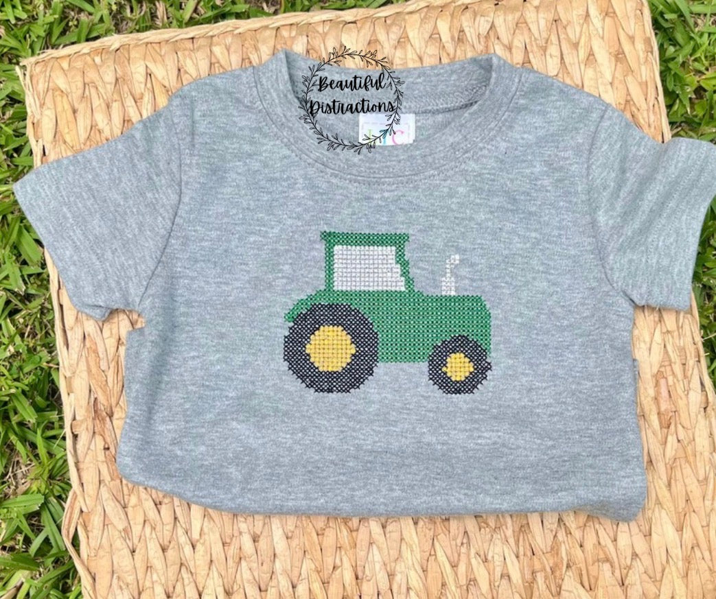 grey child tee with embroidered cross stitch detail green tractor lying on whicker platter and has beautiful distractions decal on it