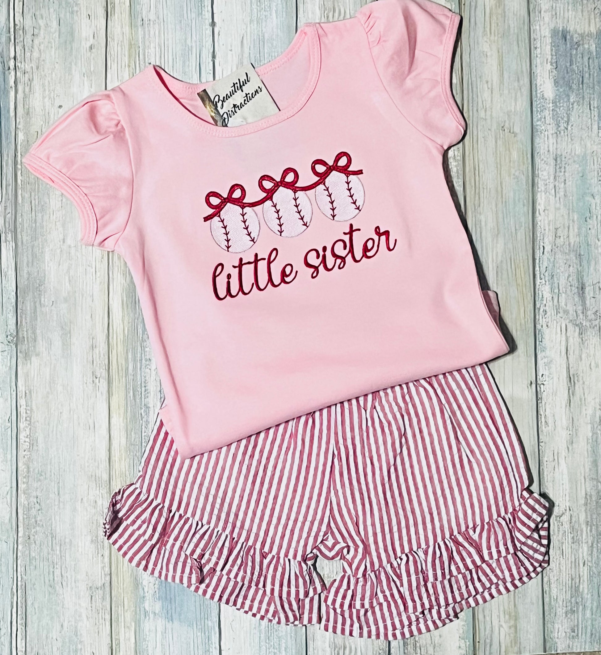pink puff sleeve top with baseballs and bows embroidered across front   says little sister underneath but can be changed to other wordings if wanted