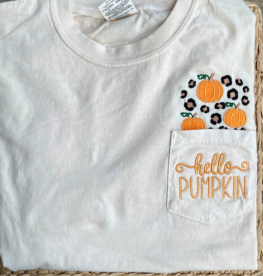 Comfort colors short sleeve pocket tee in the color ivory with 
Embroidered pumpkins and leopard spots above the pocket with hello pumpkin embroidered on the pocket area lying on woven surface

Pocket will be sewn shut

Personalization available - Hello pumpkin will be sewn on the pocket unless monogram is requested.
 If adding monogram list name or initials in personalization box in order of first name, last name, middle name