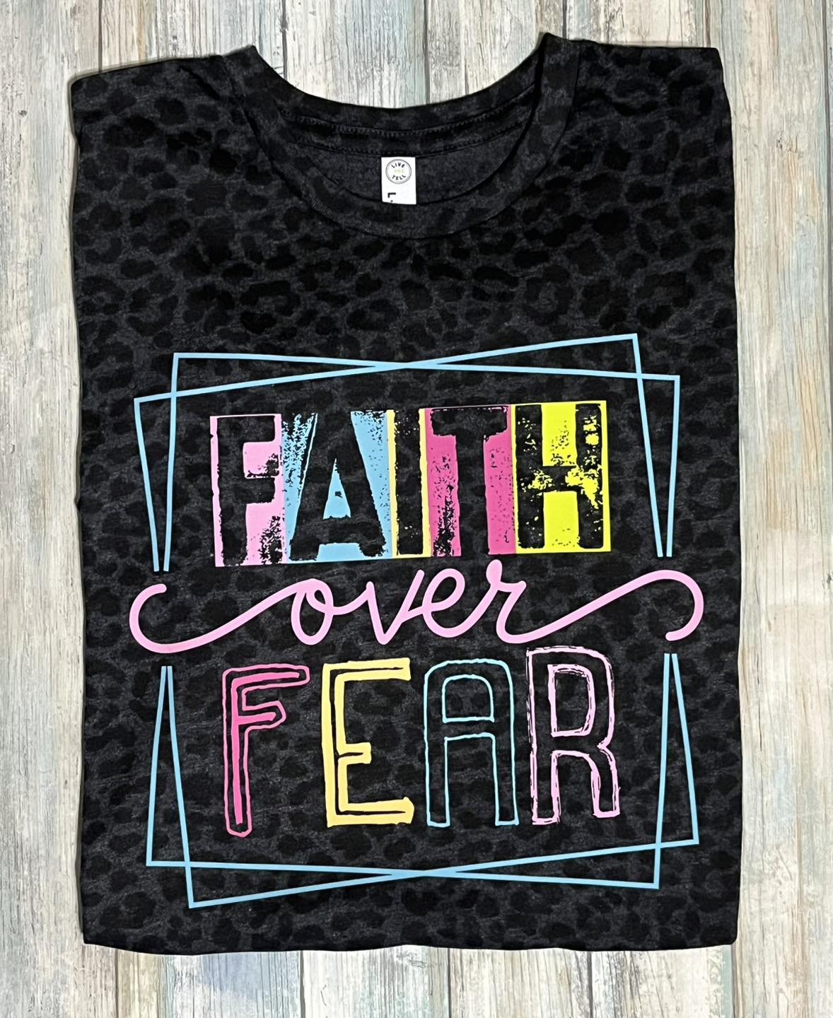 Short-sleeved black leopard print t-shirt with 'FAITH OVER FEAR' text in colorful letters on the front.