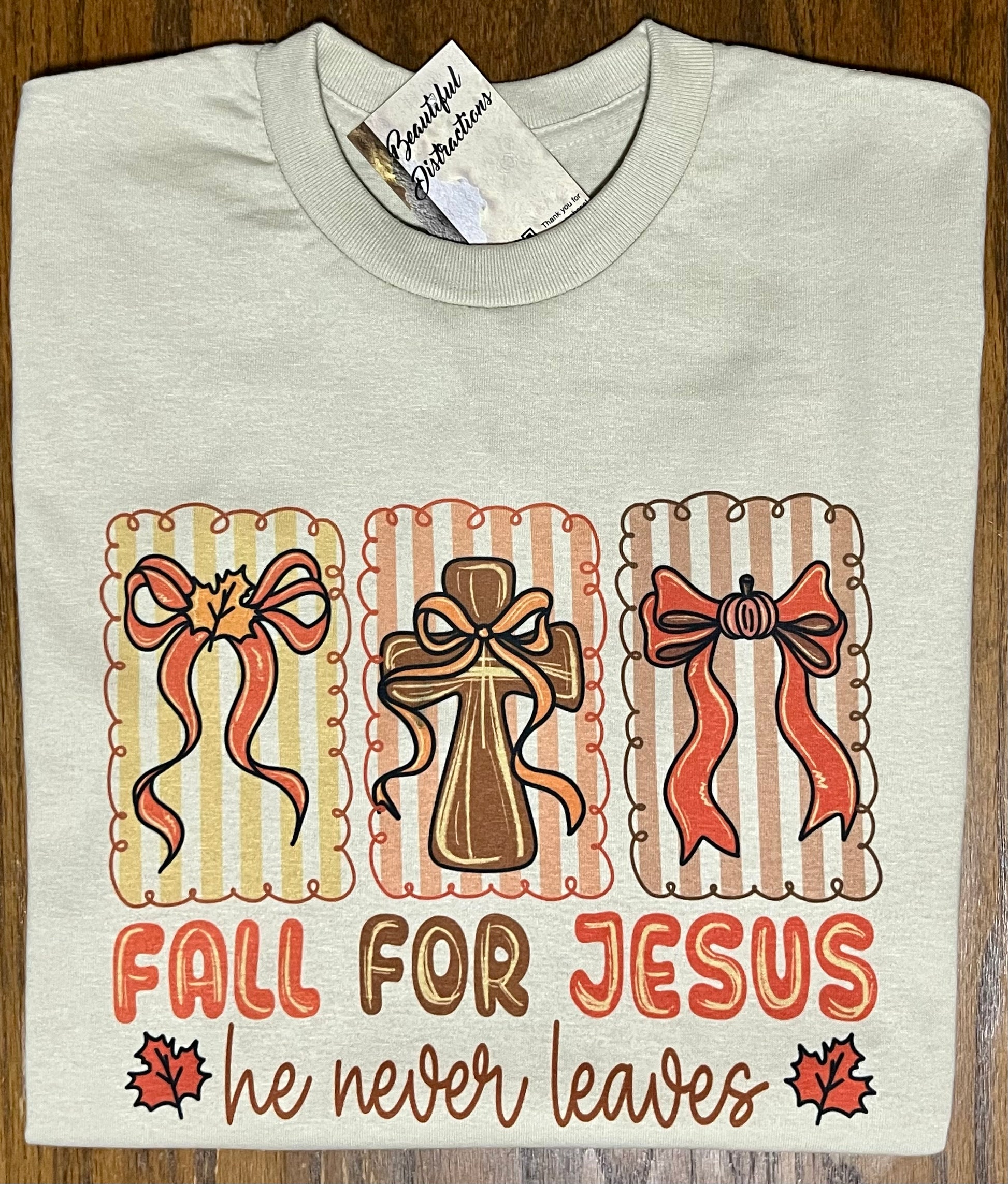 light tan shirt with 'Fall for Jesus he never leaves' design on a wooden surface