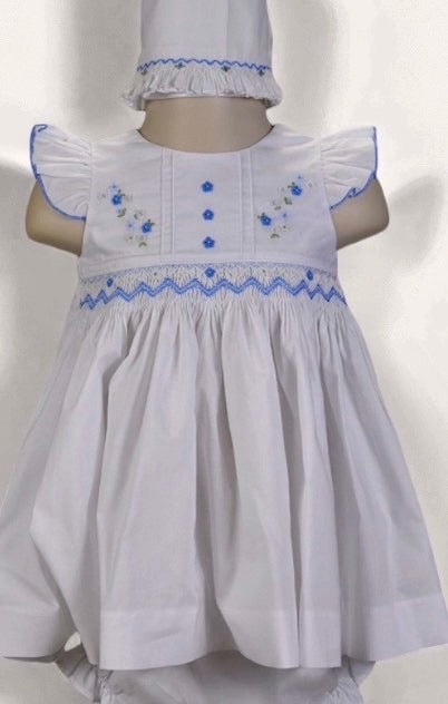 A white baby girl's dress with blue embroidered details and a matching white bonnet and bloomers, displayed on a mannequin against a white background.