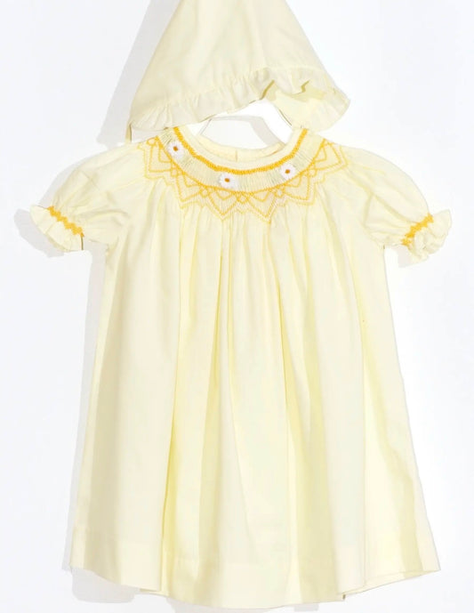 A pale yellow baby dress with a matching bonnet and bloomers  featuring yellow embroidered detailing around the collar and small daisy flowers and yellow ruffle trim on the short sleeves, displayed on a white hanger against a white background.
