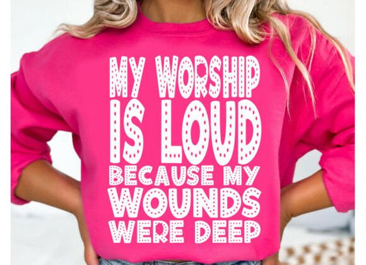 Person wearing a pink sweatshirt with text 'My worship is loud because my wounds were deep'.