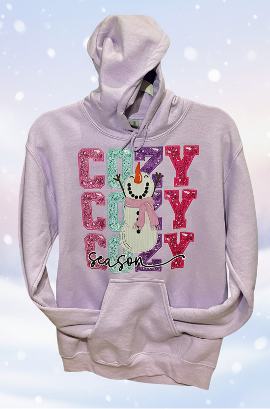 orchid color hoodie with a faux glitter decal consisting of a whimsical snowman and the word cozy stacked behind it in pink, aqua, purple and dk pink