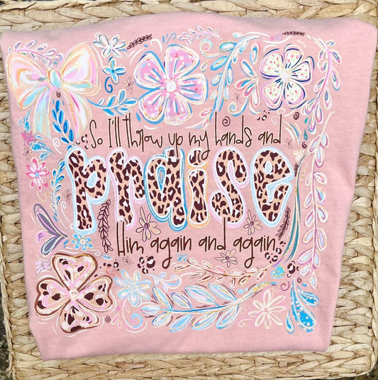 peach color tee with floral and leopard print designs that says so i'll throw up my hands and praise him again and again on a woven surface